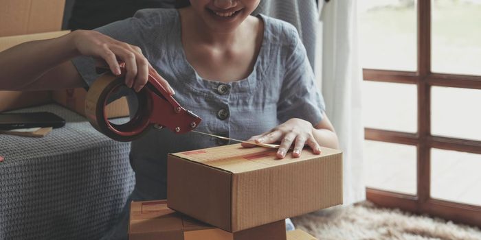 Small business entrepreneur SME, asian young woman,girl owner packing product, checking parcel for delivery to customer, using scotch tape to seal the box, working at home. Merchant online e commerce.