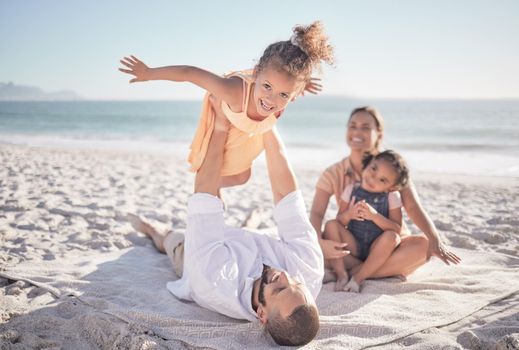 Family, children and playing with a girl on a beach holiday with her parents and sister during summer. Kids, travel and ocean with a female child or daughter on the sand by the sea with her father.