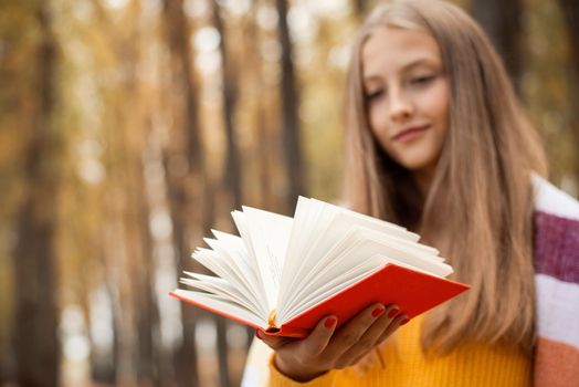 Caucasian blond girl with a book of poems having nice time in the fall park