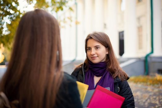 Portrait of a smiling student talking with a friend near university building, ready for studying