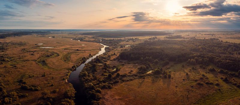 Wide panorama of small river in the countryside in the morning with rising sun on the background