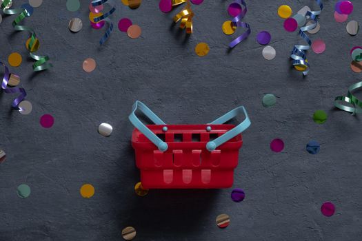 Shopping basket and festive tinsel flat lay on dark background. Top view.