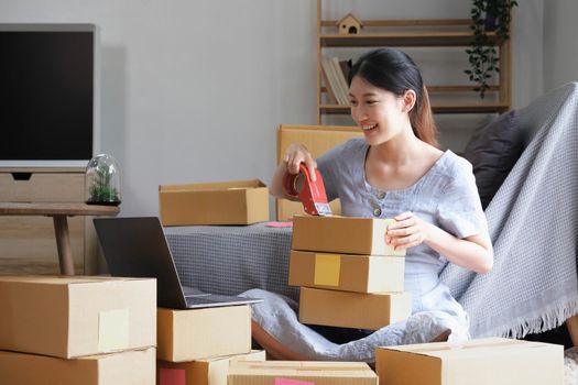 Small business entrepreneur SME, asian young woman,girl owner packing product, checking parcel for delivery to customer, using scotch tape to seal the box, working at home. Merchant online e commerce.