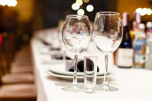 Close up new white porcelain tableware plates on purple place mats and empty wine glasses ready for dinner. Table settings wait for guests at home or restaurant