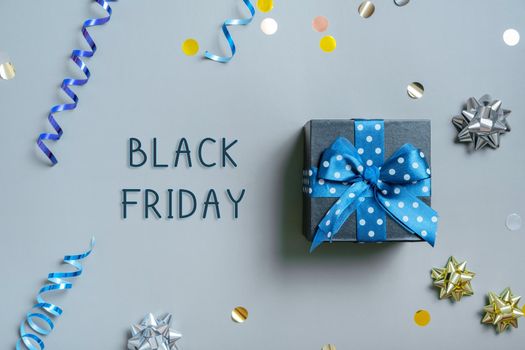 Black Friday text with gift box and festive tinsel flat lay on grey background. Top view.