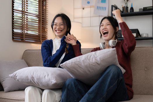 Two Young woman cheering together for sport on TV in cozy living room at home.