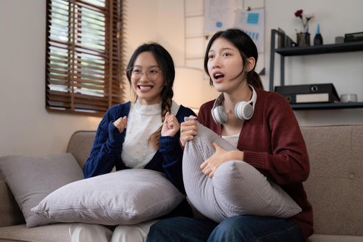 Two Young woman cheering together for sport on TV in cozy living room at home.