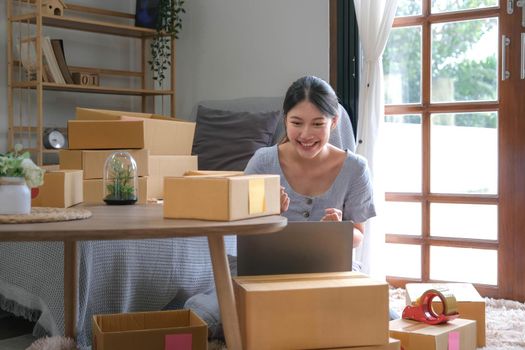 Startup SME small business entrepreneur SME or freelance Asian woman using a laptop with box, Young success Asian woman with her hand lift up, online marketing packaging box and delivery, SME concept..