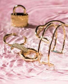 Jewellery branding, fashion gift and luxe shopping concept - Golden bracelets, earrings, rings, jewelery on pink water background, luxury glamour and holiday beauty design for jewelry brand ads