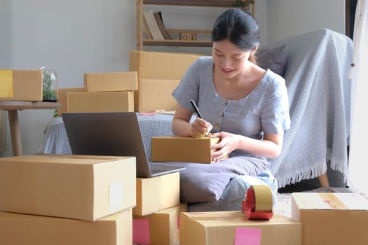 Shipping shopping online ,young start up small business owner writing address on cardboard box at workplace.small business entrepreneur SME or freelance asian woman working with box at home.