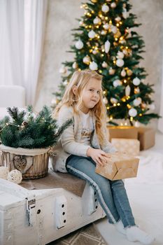 A blonde girl with a Christmas gift in her hands, on the background of a Christmas tree.The concept of New Year's decor and New Year's holidays.