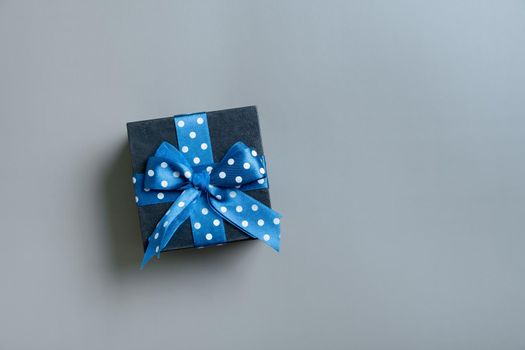 Black gift box with bow flat lay on grey background. View from above. Copy space.