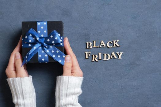 Black Friday text with gift in female hands flat lay on dark cement background. Top view.