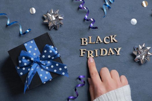 Black Friday text and female hand with gift and holiday tinsel flat lay flat lay on dark cement background. Top view.