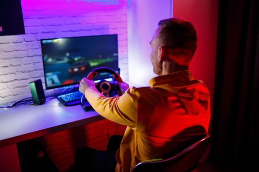 Male gamer playing racing games on the computer. He uses the steering wheel. Emotional game