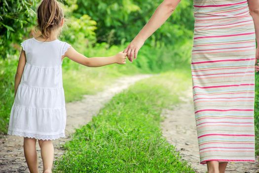 Mom and daughter are walking along the road holding hands.