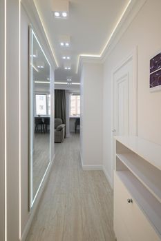 White long narrow hallway with a mirror and a couch in it and a chair in the corner of the room