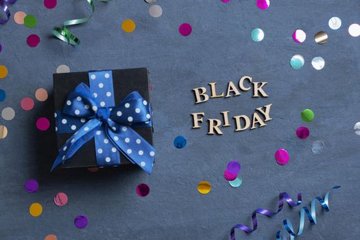 Black Friday text with gift and holiday tinsel flat lay on dark cement background. Top view.