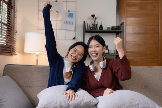 Two Young woman cheering together for sport on TV in cozy living room at home.