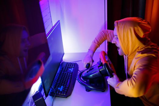 Male gamer playing racing games on the computer. He uses the steering wheel. Emotional game
