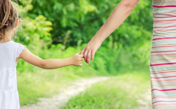 Mom and daughter are walking along the road holding hands.