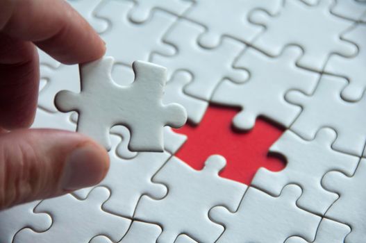 Hand holding white jigsaw puzzle on red cover background with customizable space for text. Copy space and puzzle concept.