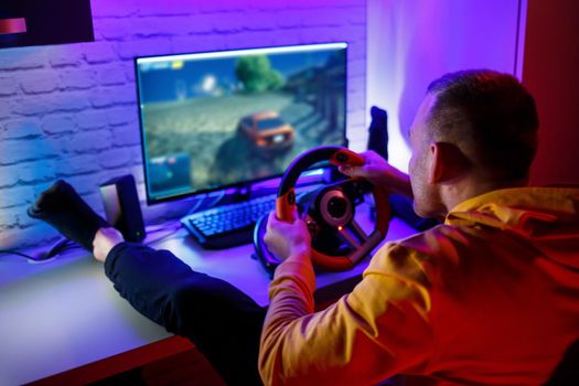 Male gamer playing racing games on the computer. He uses the steering wheel. Emotional game