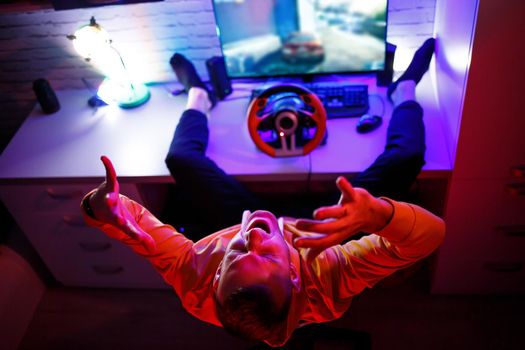 Male gamer playing racing games on the computer. He uses the steering wheel. Emotional game