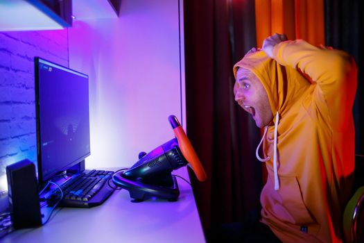 Male gamer playing racing games on the computer. He uses the steering wheel. Emotional game