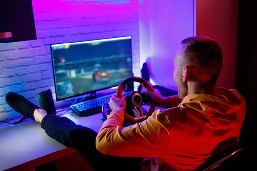 Male gamer playing racing games on the computer. He uses the steering wheel. Emotional game