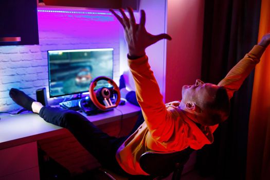 Male gamer playing racing games on the computer. He uses the steering wheel. Emotional game