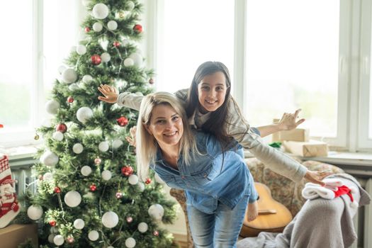 Mother with her child daughter celebrating near Christmas tree.