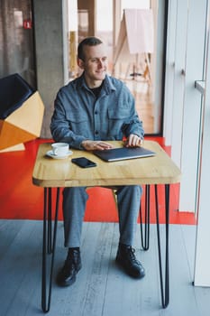 Handsome male manager sits at a table in a modern office with a closed laptop and rests, remote work