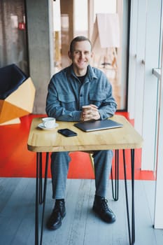 Handsome male manager sits at a table in a modern office with a closed laptop and rests, remote work