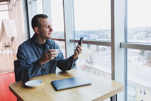 Happy smiling male manager sitting in cafe using mobile phone gadget, ordering delivery service via online app, free 4g wireless network in cafe, cheerful freelancer texting on mobile phone