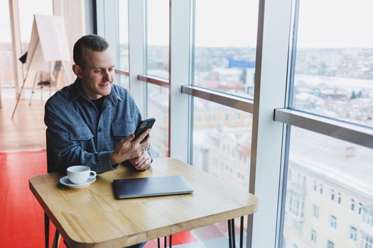 Happy smiling male manager sitting in cafe using mobile phone gadget, ordering delivery service via online app, free 4g wireless network in cafe, cheerful freelancer texting on mobile phone