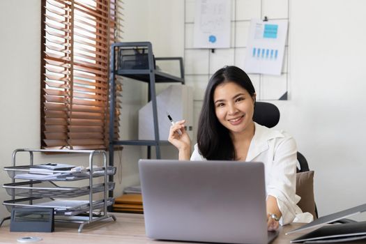 Photo of joyful nice woman using laptop and smiling while sitting at office