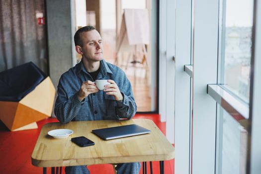 Cheerful IT professional with laptop talking on smartphone to discuss web programming, happy businessman in cafe drinking coffee. freelancer