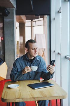 Happy smiling male manager sitting in cafe using mobile phone gadget, ordering delivery service via online app, free 4g wireless network in cafe, cheerful freelancer texting on mobile phone