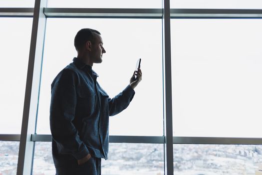 Young business man holding a phone. In an office or business center against the background of large windows of a skyscraper. Work and career, concept