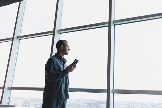 Young business man holding a phone. In an office or business center against the background of large windows of a skyscraper. Work and career, concept