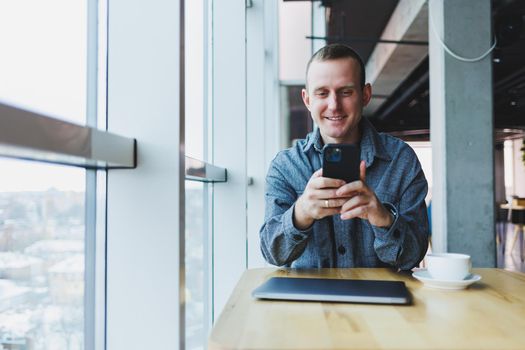 Happy smiling male manager sitting in cafe using mobile phone gadget, ordering delivery service via online app, free 4g wireless network in cafe, cheerful freelancer texting on mobile phone