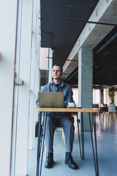 A young successful businessman in a suit drinks coffee and works in a cafe on wireless free internet on a laptop, sitting alone at a table in a cafe.
