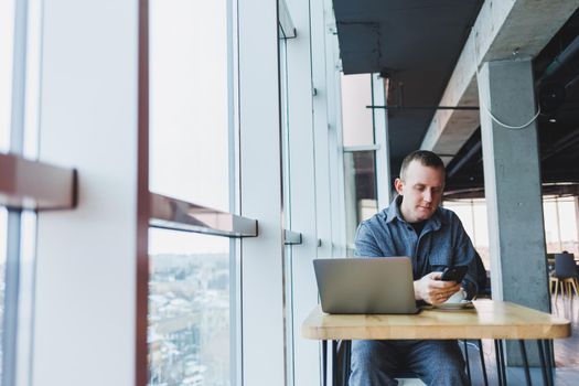 Confident male manager sits at a table in a modern office at a laptop and works, he is talking on the phone, remote work