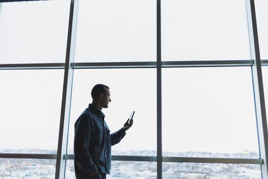 Young business man holding a phone. In an office or business center against the background of large windows of a skyscraper. Work and career, concept