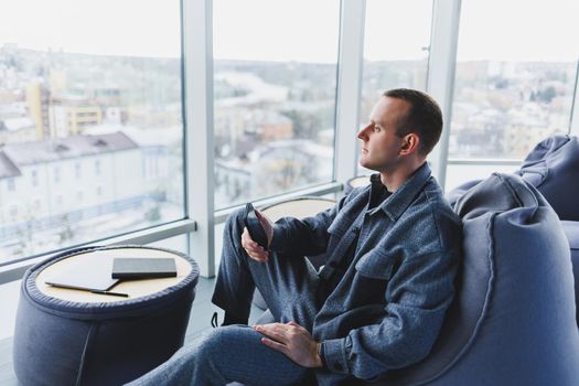 Confident male manager sitting in a modern workspace at a laptop and talking on the phone, remote work