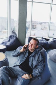 Confident male manager sitting in a modern workspace at a laptop and talking on the phone, remote work