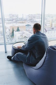 Break. Smiling young man relaxing on bean bag chair while sitting at table and relaxing using laptop, happy businessman leaning back, enjoying work, feeling satisfied