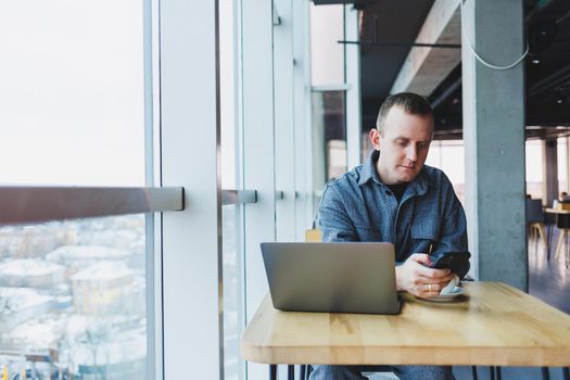 Confident male manager sits at a table in a modern office at a laptop and works, he is talking on the phone, remote work