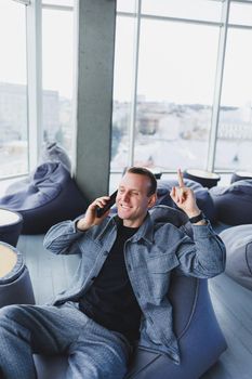 Confident male manager sitting in a modern workspace at a laptop and talking on the phone, remote work